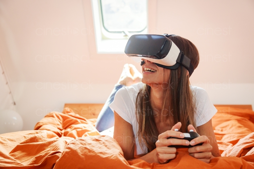 Frau mit VR-Brille und Joypad auf dem Bett 20160810