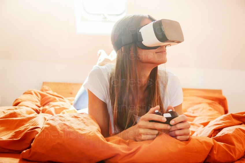 Frau mit VR-Brille und Joypad auf dem Bett 20160810