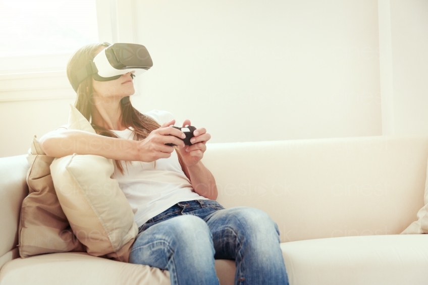 Frau mit VR-Brille und Joypad auf dem Sofa 20160810