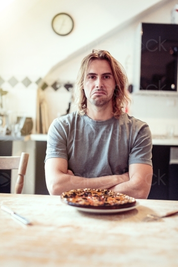 Mann sitzt vor Teller mit einer verbrannten Pizza 20160810